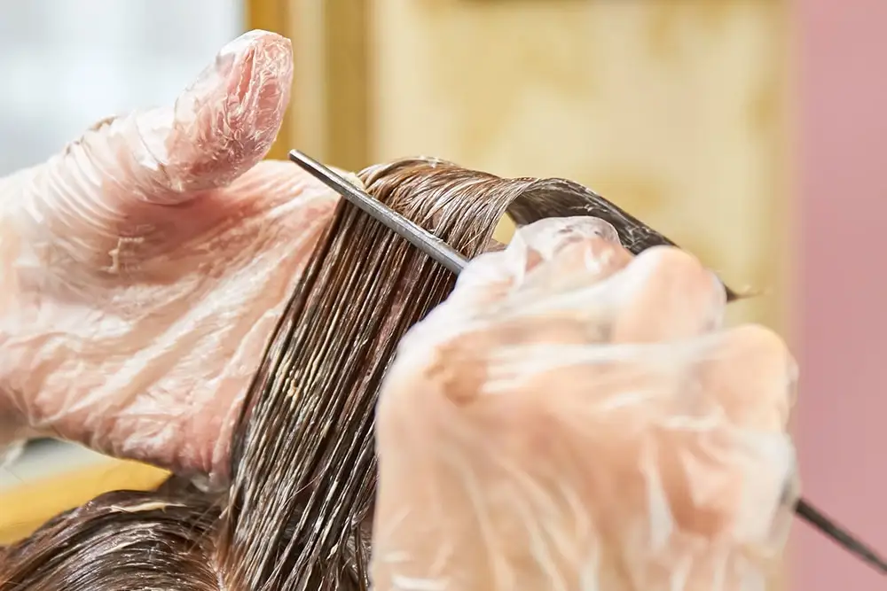 Stylist's gloved hands applying color to a section of hair