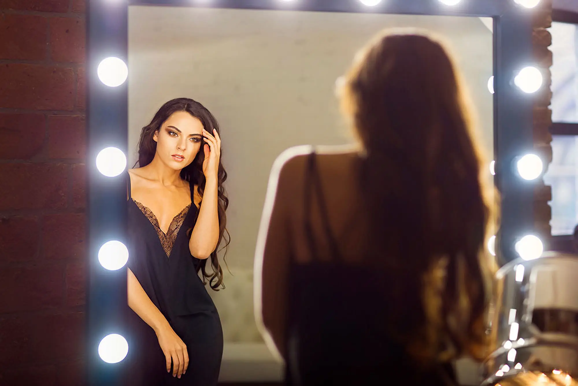 Woman in an evening dress posing in front of a lighted mirror